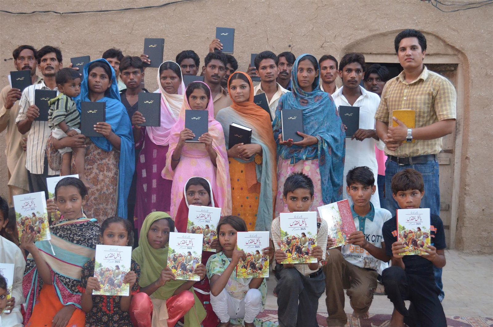 Children in Pakistan holding up the illustrated Urdu Bibles they have just received