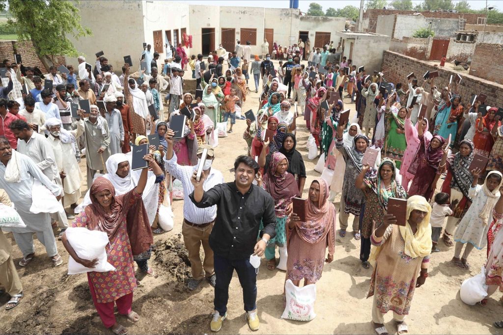 Villagers in Pakistan with raised hands at a free Urdu Bible distribution in their village